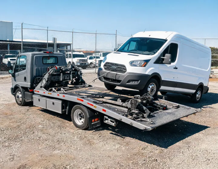 Custom flatbed tow truck loading a commercial van in a fleet recovery yard